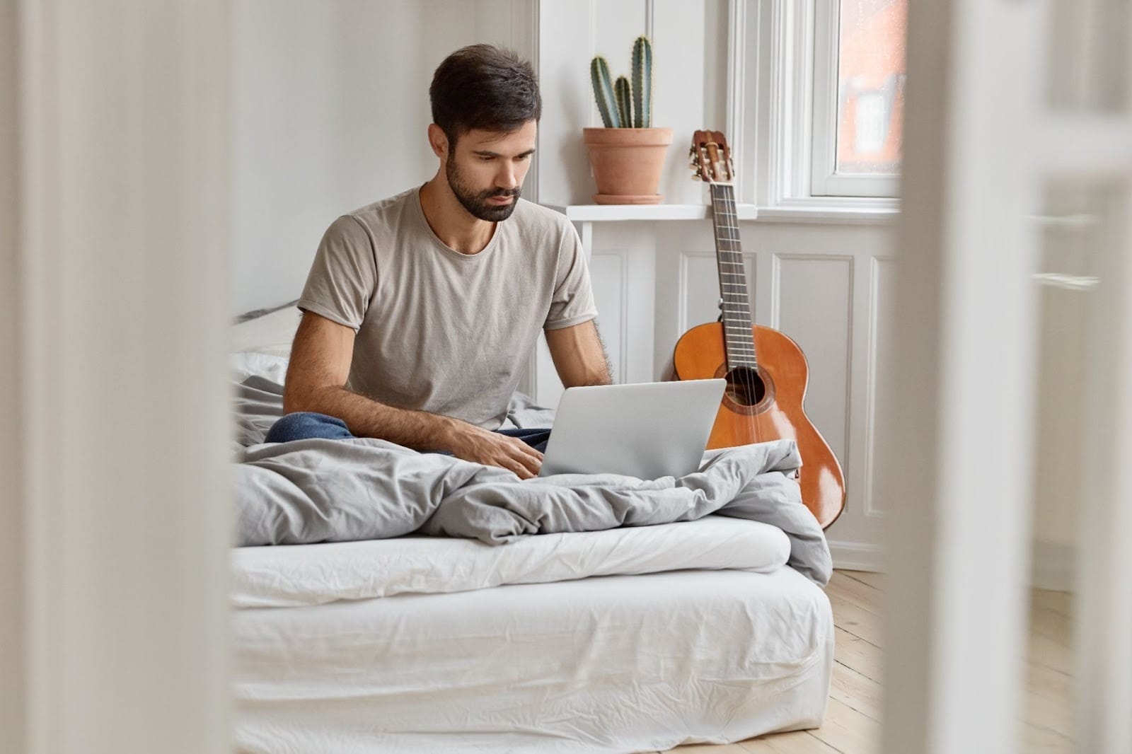 A man sitting on a bed and using a laptop in a cozy room setting